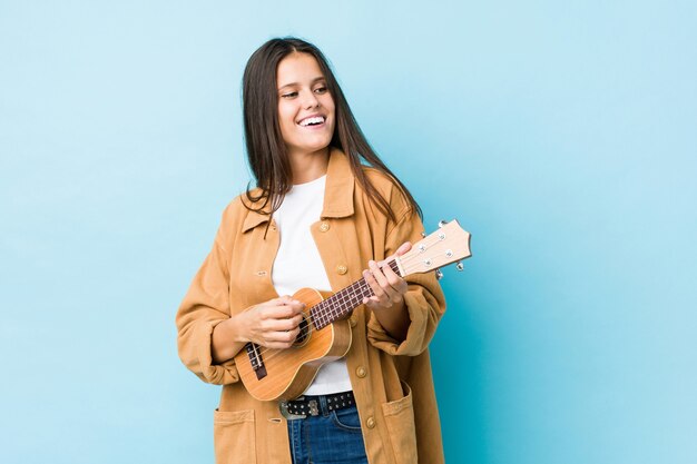 Junge kaukasische Frau, die Ukelele spielt, lokalisiert auf einer blauen Wand