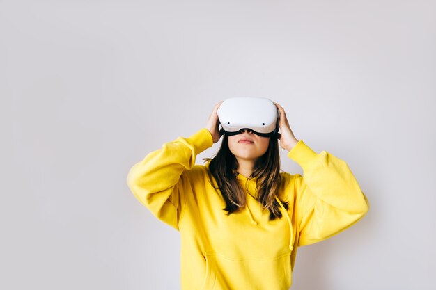 Junge kaukasische Frau, die VR-Headset verwendet, Brille berührt und in der virtuellen Realität auf weißem Hintergrund nachschaut.