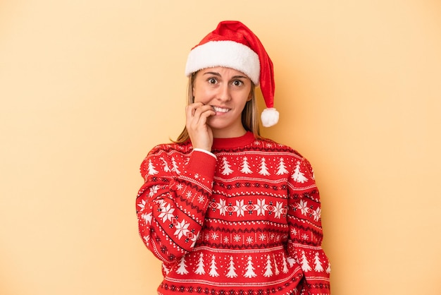 Junge kaukasische Frau, die Weihnachten isoliert auf gelbem Hintergrund feiert, beißt Fingernägel, nervös und sehr ängstlich.