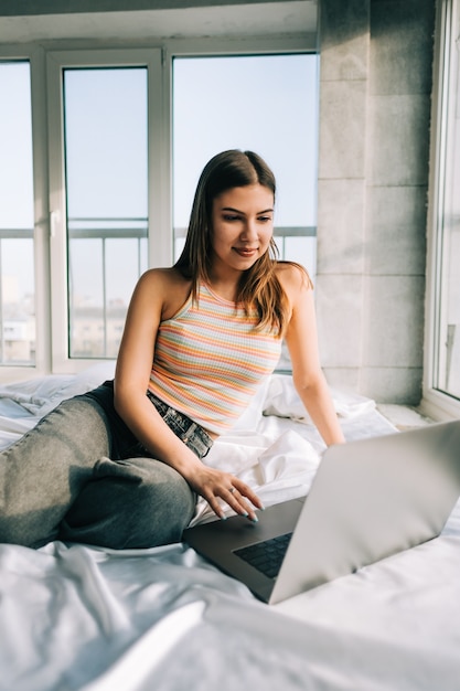 Junge kaukasische Frau, die zu Hause auf einem Bett ruht und Laptop verwendet