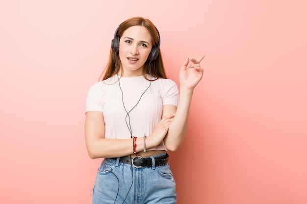 Junge kaukasische Frau hören das Musiklächeln, das freundlich mit dem Zeigefinger weg zeigt.