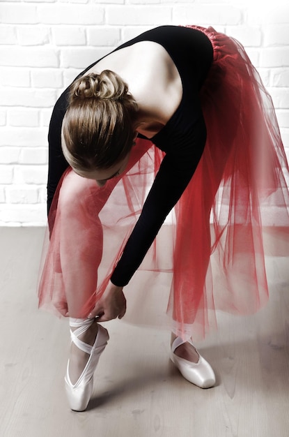 Junge kaukasische Frau im Ballettröckchen, die ihre Spitzen auf weißem Backsteinmauerhintergrund schnürt