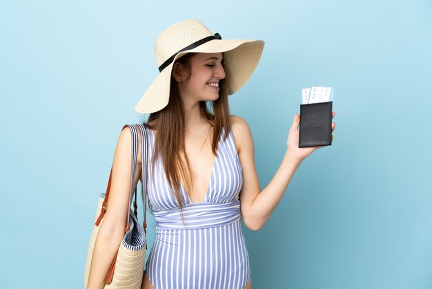 Junge kaukasische Frau in den Sommerferien mit Reisepass auf blauem Hintergrund mit glücklichem Ausdruck isoliert