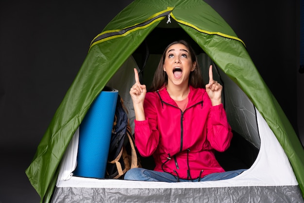 Junge kaukasische Frau in einem grünen Zelt des Campings überrascht und zeigt nach oben