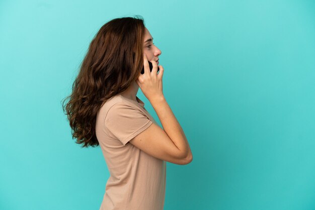 Junge kaukasische Frau isoliert auf blauem Hintergrund, die ein Gespräch mit dem Handy mit jemandem führt