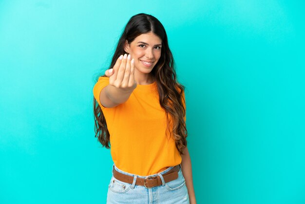 Junge kaukasische Frau isoliert auf blauem Hintergrund, die einlädt, mit der Hand zu kommen. Schön, dass du gekommen bist