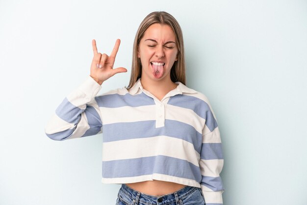 Junge kaukasische Frau isoliert auf blauem Hintergrund, die Rockgeste mit den Fingern zeigt