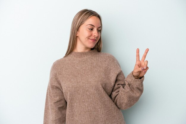 Junge kaukasische Frau isoliert auf blauem Hintergrund fröhlich und sorglos, die ein Friedenssymbol mit den Fingern zeigt.