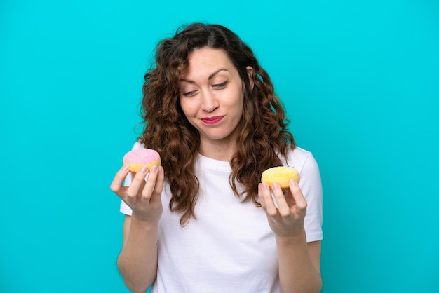 Junge kaukasische Frau isoliert auf blauem Hintergrund mit Donuts