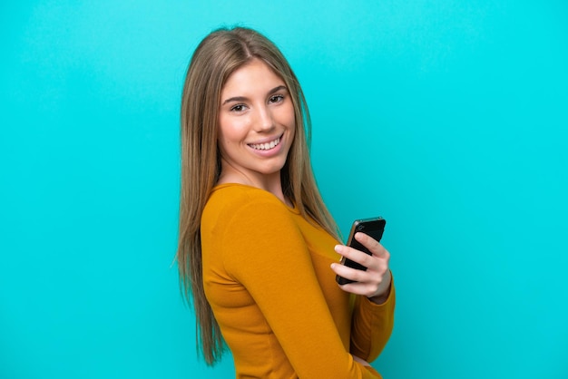 Junge kaukasische Frau isoliert auf blauem Hintergrund mit einem Handy und verschränkten Armen