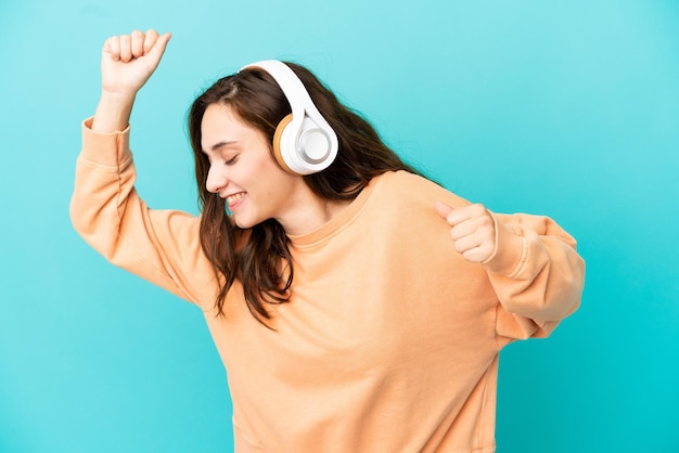 Junge kaukasische Frau isoliert auf blauem Hintergrund Musik hören und tanzen