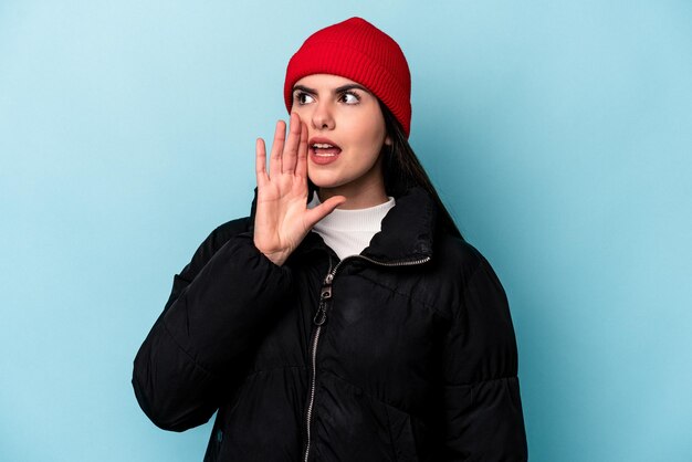 Junge kaukasische Frau isoliert auf blauem Hintergrund schreit und hält Handfläche in der Nähe des geöffneten Mundes