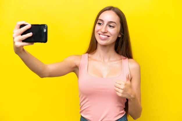 Junge kaukasische Frau isoliert auf gelbem Hintergrund, die ein Selfie mit dem Handy macht