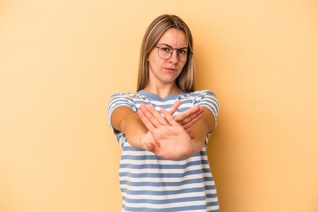 Junge kaukasische Frau isoliert auf gelbem Hintergrund, die mit ausgestreckter Hand steht und Stoppschild zeigt und Sie verhindert.