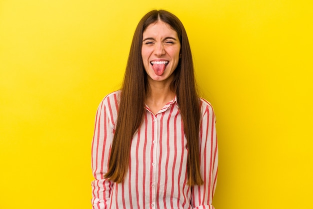Junge kaukasische Frau isoliert auf gelbem Hintergrund lustig und freundlich, die Zunge herausstrecken.