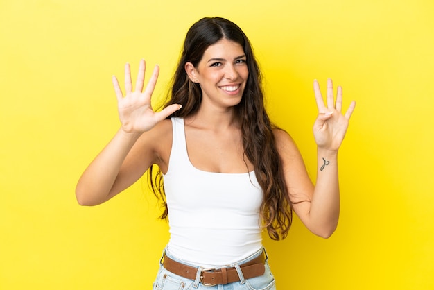 Junge kaukasische Frau isoliert auf gelbem Hintergrund und zählt neun mit den Fingern