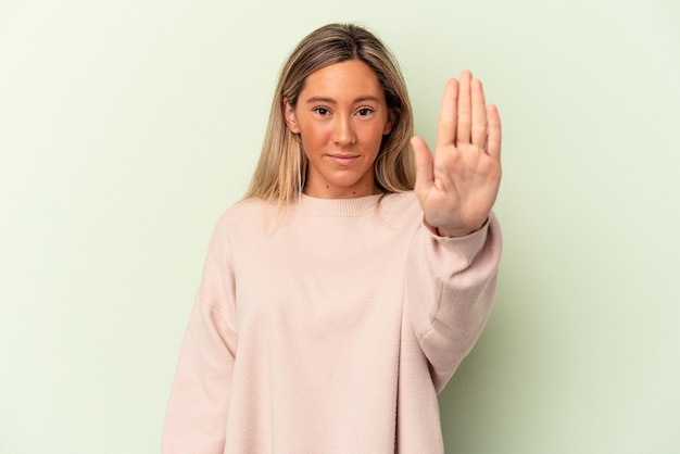 Junge kaukasische Frau isoliert auf grünem Hintergrund, die mit ausgestreckter Hand steht und Stoppschild zeigt und Sie verhindert.