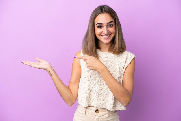 Junge kaukasische Frau isoliert auf lila Hintergrund, die Kopienraum imaginär auf der Handfläche hält, um eine Anzeige einzufügen