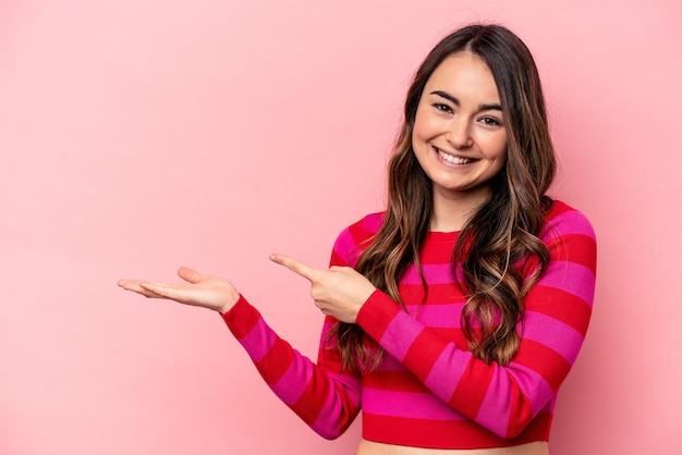 Junge kaukasische Frau isoliert auf rosa Hintergrund aufgeregt mit einem Kopierraum auf der Handfläche