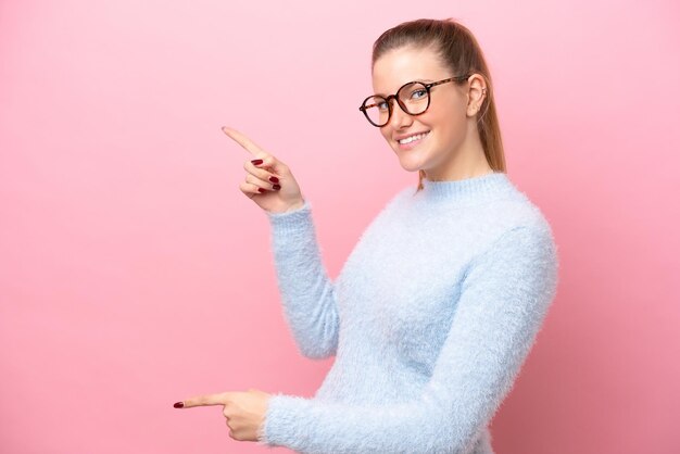 Junge kaukasische Frau isoliert auf rosa Hintergrund, die mit dem Finger zur Seite zeigt und ein Produkt präsentiert