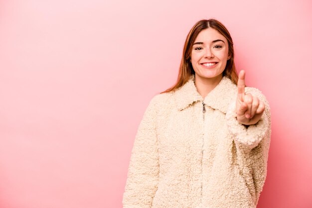 Junge kaukasische Frau isoliert auf rosa Hintergrund, die Nummer eins mit dem Finger zeigt