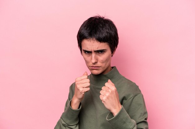 Junge kaukasische Frau isoliert auf rosafarbenem Hintergrund, die der Kamera die Faust zeigt, aggressiver Gesichtsausdruck.