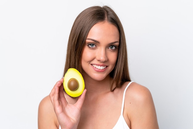 Junge kaukasische Frau isoliert auf weißem Hintergrund, die eine Avocado hält, während sie lächelt Close up Portrait