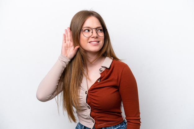 Foto junge kaukasische frau isoliert auf weißem hintergrund, die etwas hört, indem sie die hand auf das ohr legt