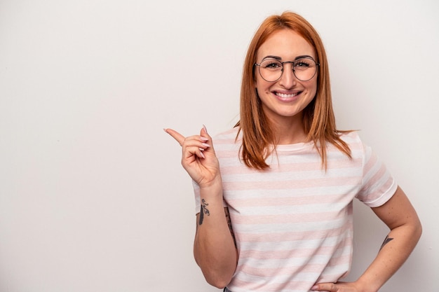 Junge kaukasische Frau isoliert auf weißem Hintergrund, die fröhlich lächelt und mit dem Zeigefinger wegzeigt