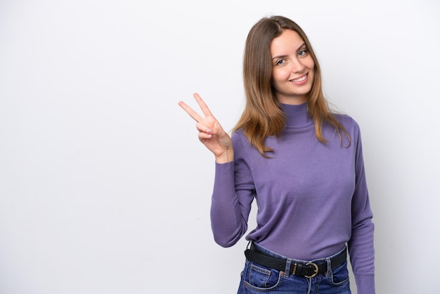 Junge kaukasische Frau isoliert auf weißem Hintergrund lächelt und zeigt Victory-Zeichen