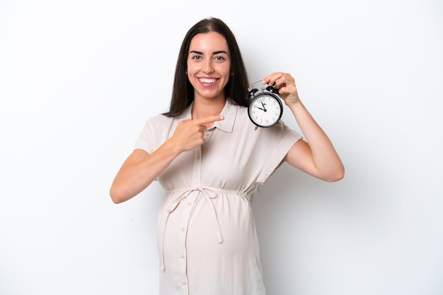 Junge kaukasische Frau isoliert auf weißem Hintergrund schwanger und hält Uhr