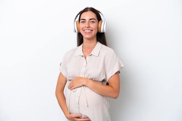 Junge kaukasische Frau isoliert auf weißem Hintergrund schwanger und Musik hören