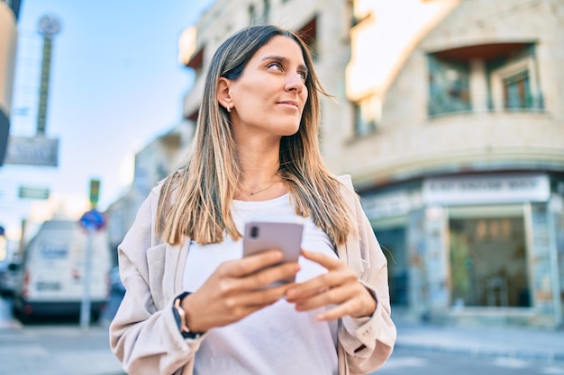 Junge kaukasische Frau lächelt glücklich und nutzt ihr Smartphone in der Stadt