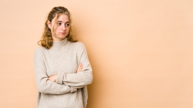 Junge kaukasische Frau lokalisiert auf beige Wand verdächtig, unsicher, Sie untersuchend.