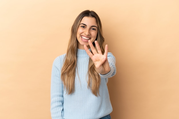 Junge kaukasische Frau lokalisiert auf beigem Hintergrund glücklich und zählt vier mit den Fingern