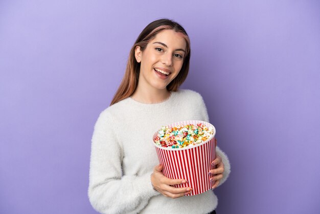 Junge kaukasische Frau lokalisiert auf Blau, das einen großen Eimer Popcorn hält