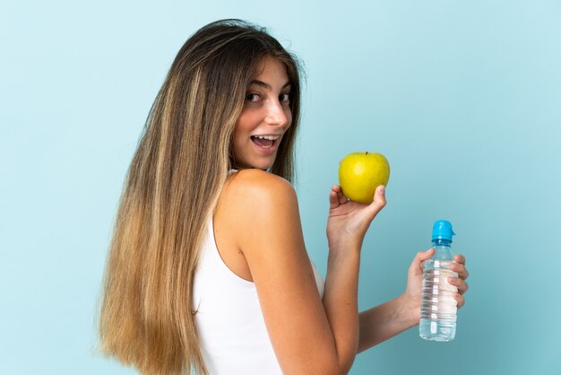 Junge kaukasische Frau lokalisiert auf Blau mit einem Apfel und mit einer Flasche Wasser