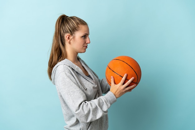 Junge kaukasische Frau lokalisiert auf blau spielendem Basketball