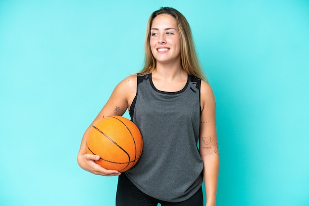 Junge kaukasische Frau lokalisiert auf blauem Hintergrund, der Basketball spielt