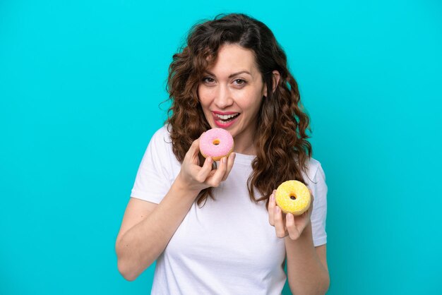 Junge kaukasische Frau lokalisiert auf blauem Hintergrund, der einen Donut hält