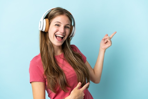 Junge kaukasische Frau lokalisiert auf blauem Hintergrund, der Musik hört und Gitarrengeste tut