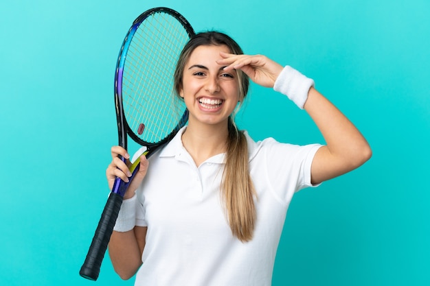 Junge kaukasische Frau lokalisiert auf blauem Hintergrund, der Tennis spielt