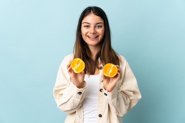 Junge kaukasische Frau lokalisiert auf blauer Wand, die eine Orange hält