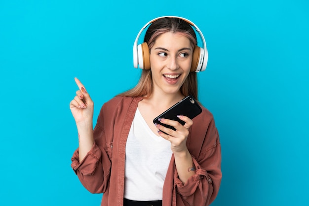 Junge kaukasische Frau lokalisiert auf blauer Wand, die Musik mit einem Handy und Gesang hört