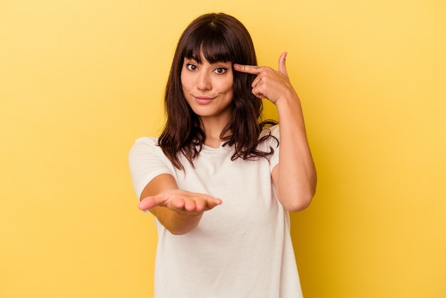 Foto junge kaukasische frau lokalisiert auf gelber wand, die ein produkt an der hand hält und zeigt.