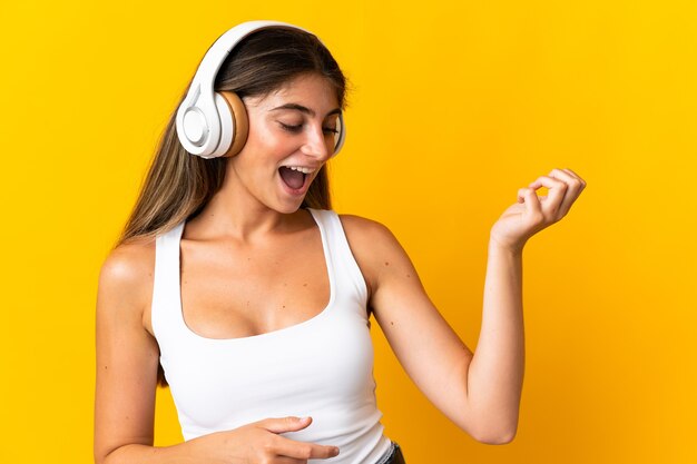 Junge kaukasische Frau lokalisiert auf gelber Wand, die Musik hört und Gitarrengeste tut