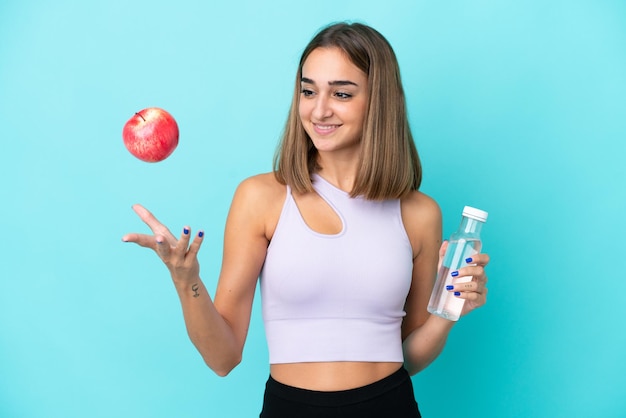 Junge kaukasische Frau lokalisiert auf lila Hintergrund mit einem Apfel und mit einer Flasche Wasser