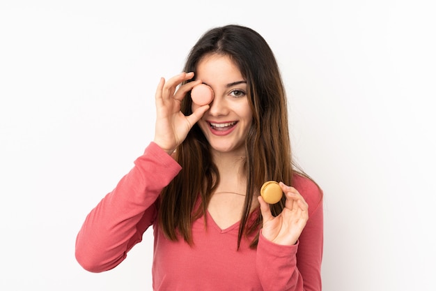 Junge kaukasische Frau lokalisiert auf rosa, die bunte französische Macarons hält