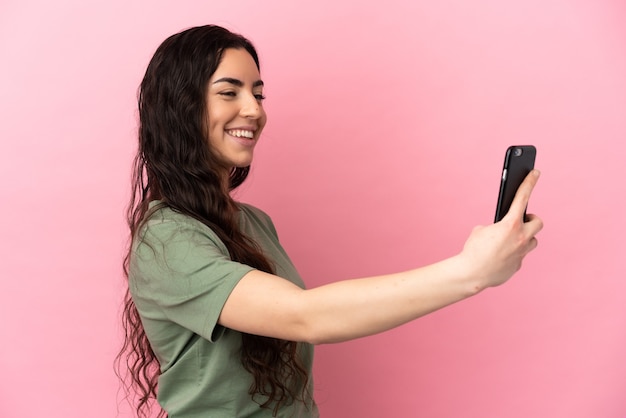 Junge kaukasische Frau lokalisiert auf rosa Hintergrund, der ein selfie mit Handy macht