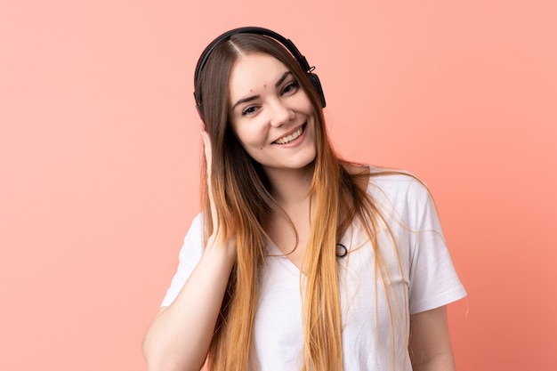 Junge kaukasische Frau lokalisiert auf rosa Wand, die Musik hört